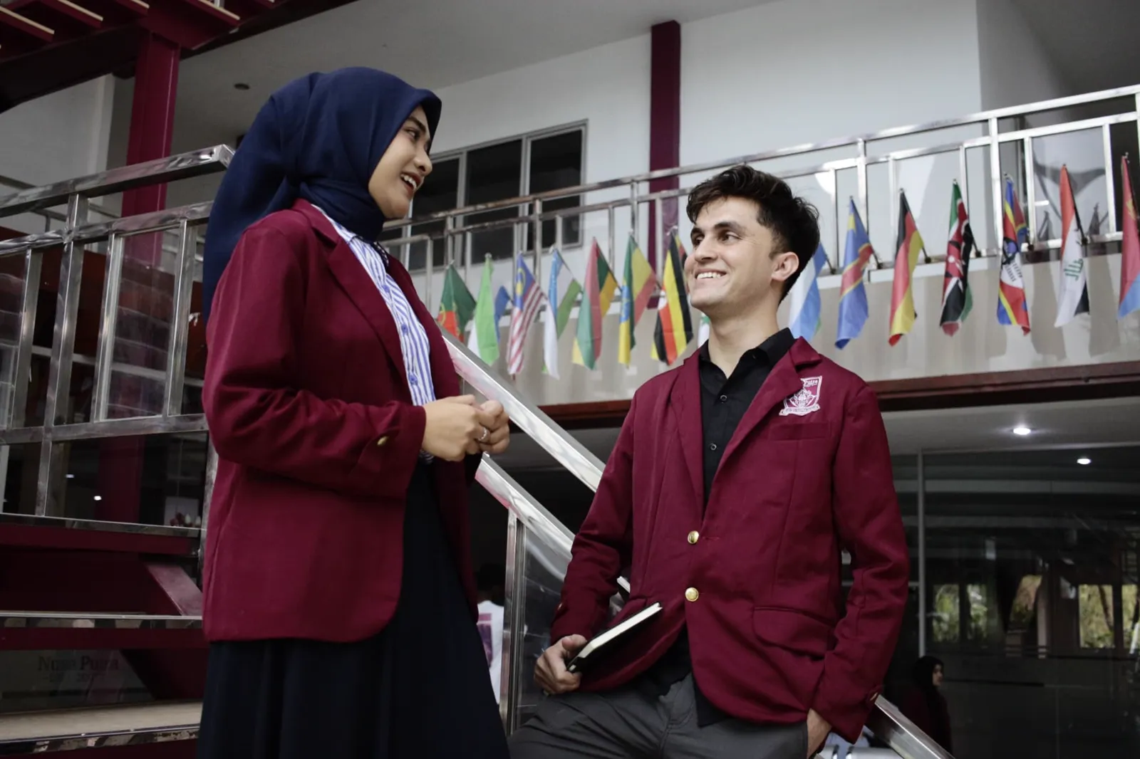 Dua mahasiswa Nusa Putra berbincang di depan deretan bendera negara asal mahasiswa internasional